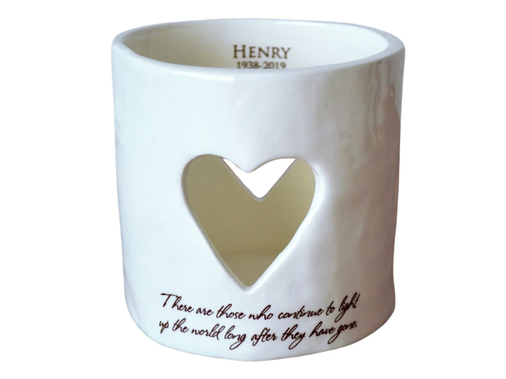 A white ceramic heart-shaped candle holder with a cut-out heart shape in the front, featuring a personalized name and date inside.