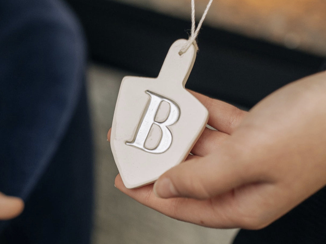 Person holding a decorative ornament with a letter 'B' on it against a blurred background