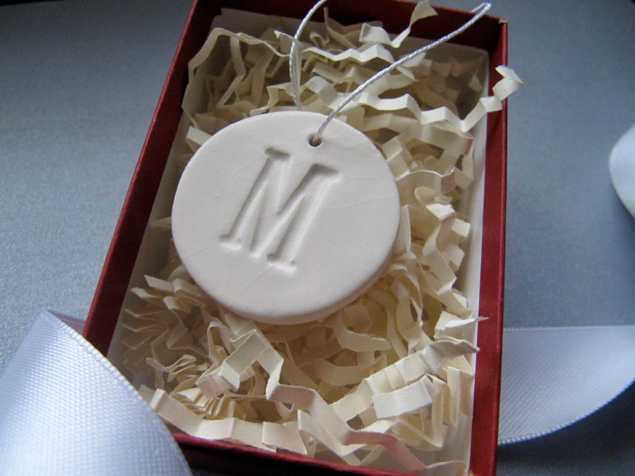 White ceramic ornament with 'M' in a red box with crinkled paper