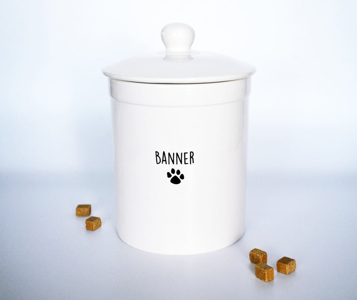 White ceramic dog treat jar with a lid and paw print design on a light blue background