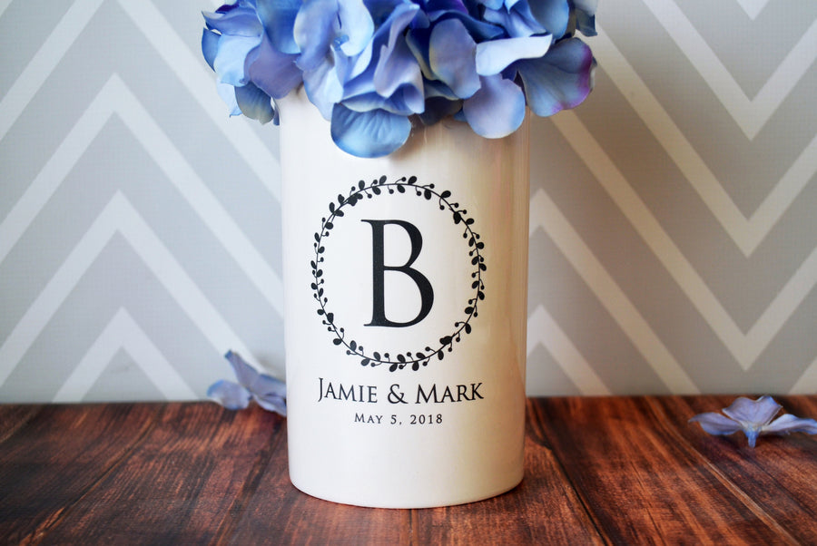 A white ceramic vase with a wreath design and a large initial in the center, personalized with the names 'Jamie and Mark' and a date 'May 9, 2019'.