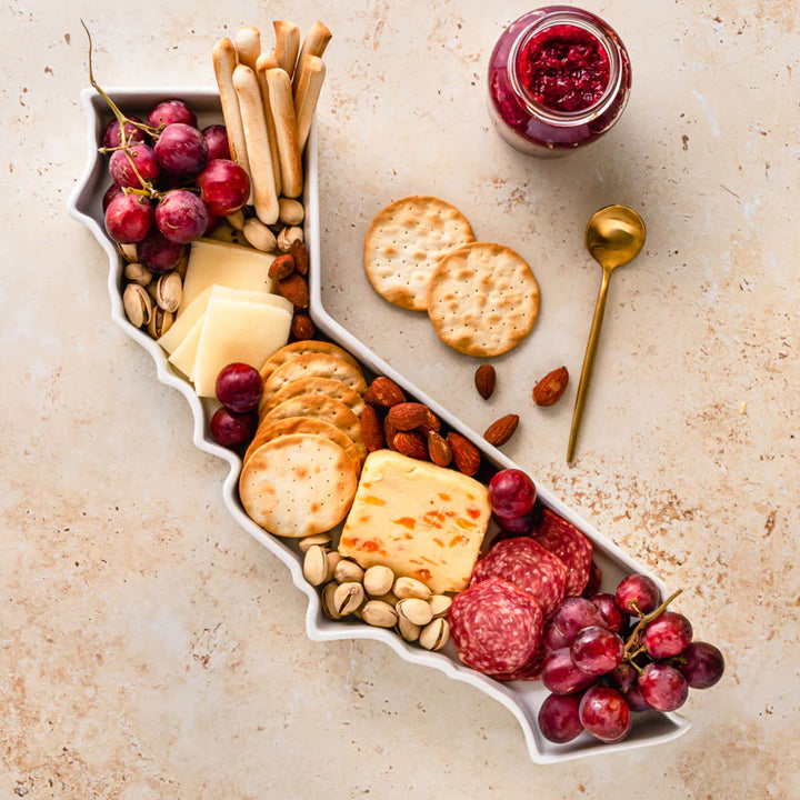 Assorted snacks including crackers, cheese, grapes, and salami on a decorative platter.