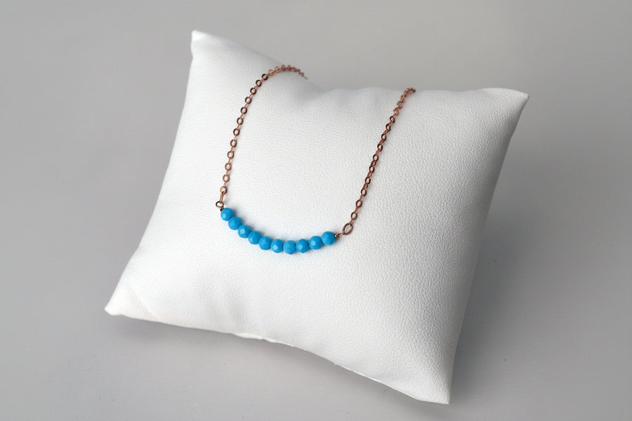 Necklace with Turquoise beads on a white pillow against a gray background