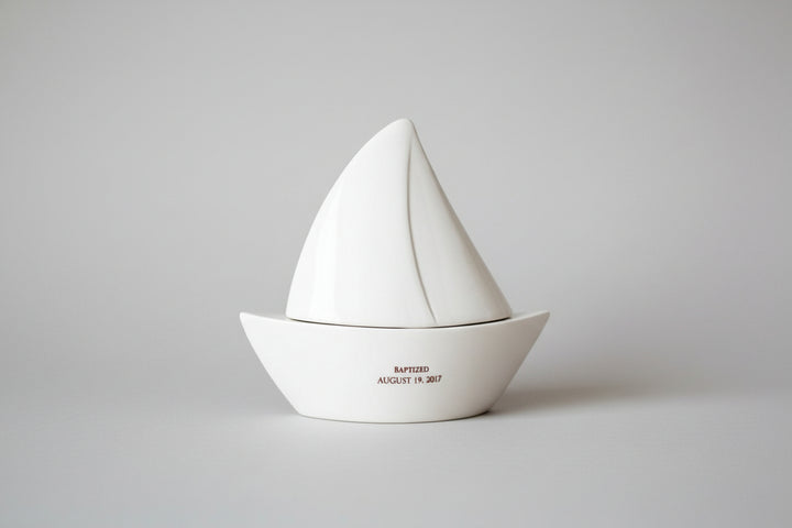 White ceramic sailboat on a wooden surface with a chevron patterned wall in the background