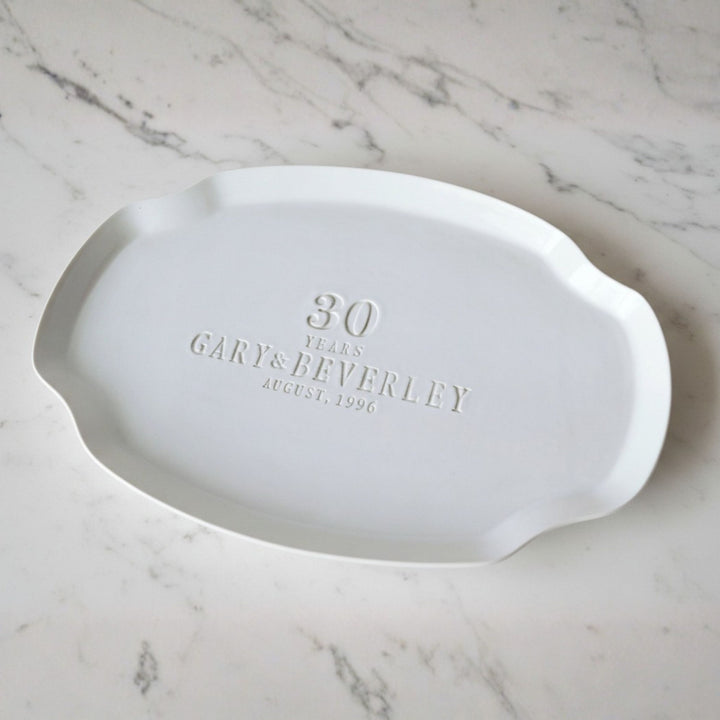 White ceramic platter with engraved text on a marble surface