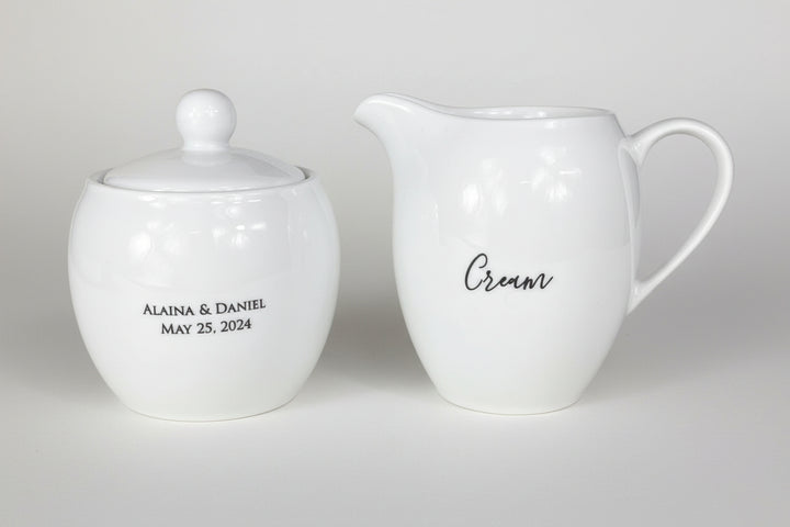 White ceramic sugar bowl and cream pitcher with personalized text on a light gray background