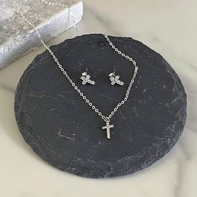 Silver cross necklace and earrings set on a dark stone surface with a light background