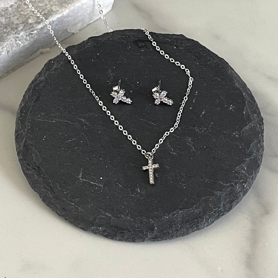 Silver necklace with cross pendant and matching earrings on a dark stone surface.
