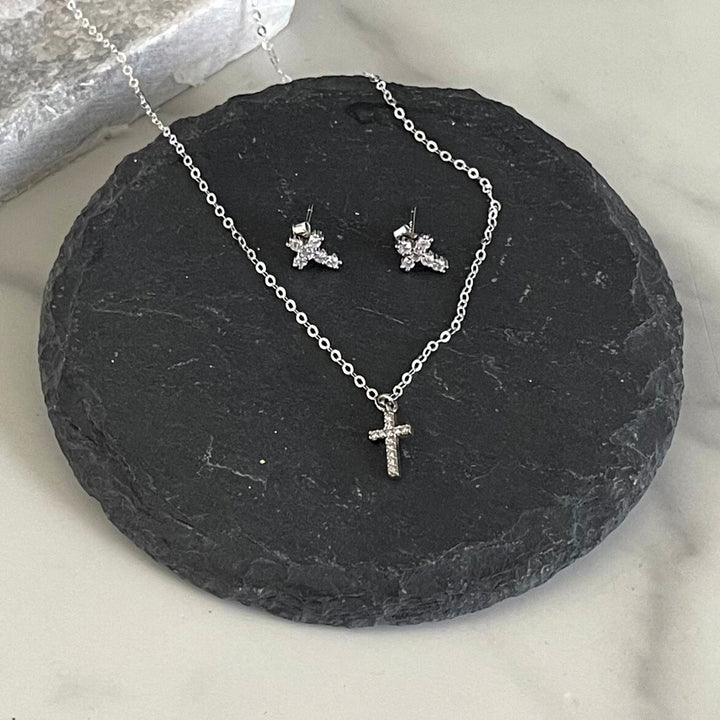 Silver necklace with cross pendant and matching earrings on a dark stone surface.