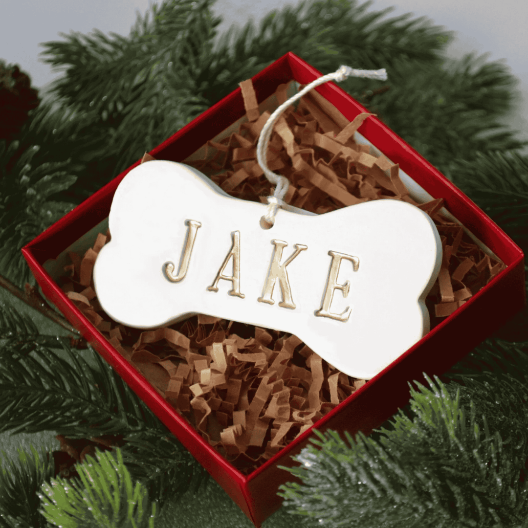 Dog bone-shaped ornament with 'JAKE' on it in a red box surrounded by greenery