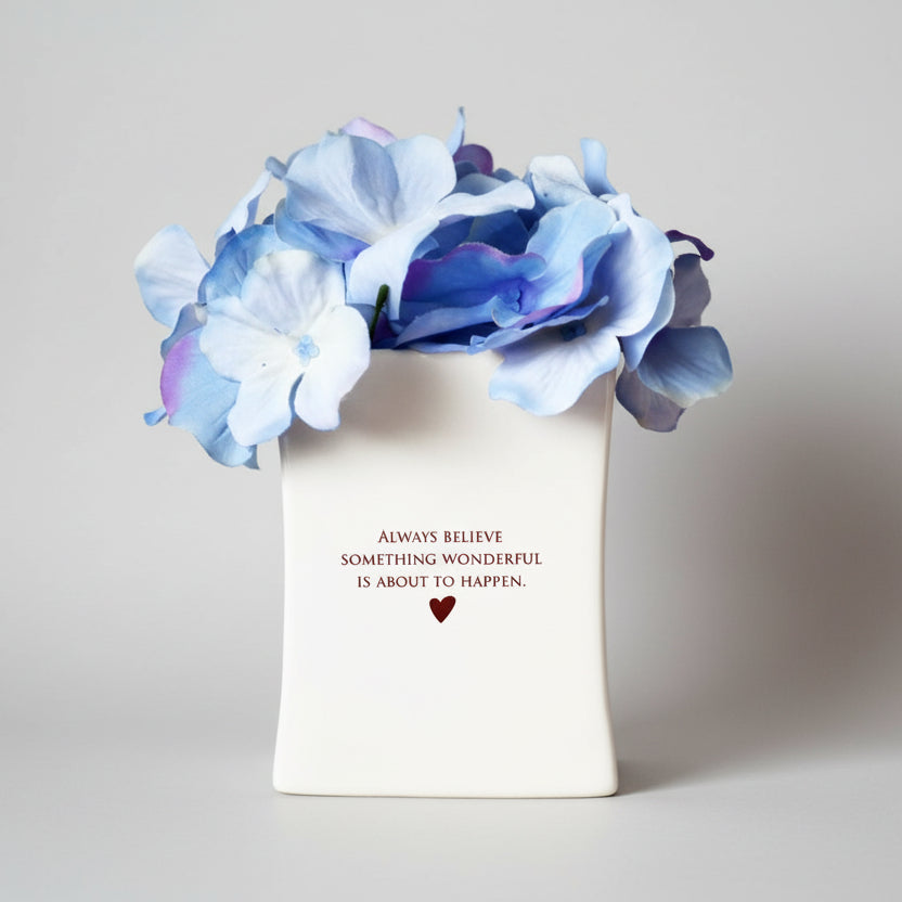 White vase with blue flowers and motivational quote.