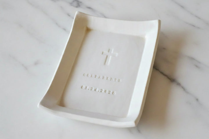 White ceramic dish with a cross and text on a wooden surface