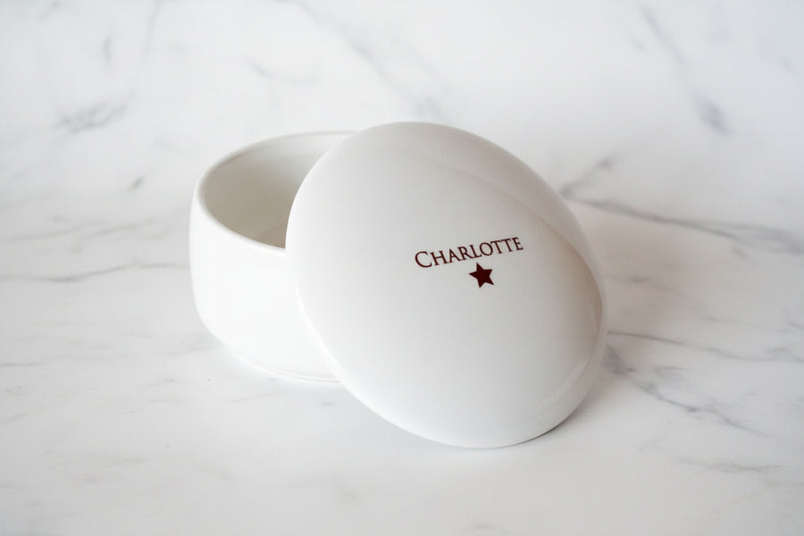 White round container with 'Charlotte' and a star on a wooden surface