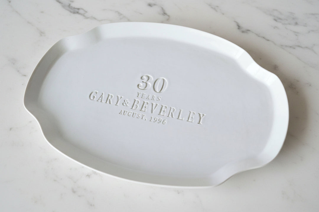White ceramic platter with engraved text on a wooden surface