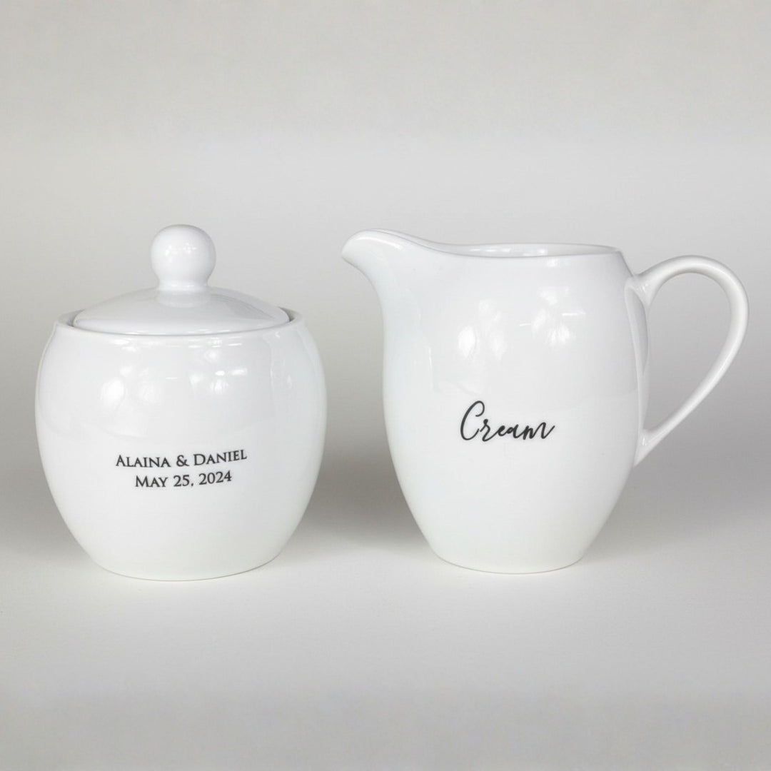 White ceramic sugar bowl and cream pitcher with personalized text on a light gray background