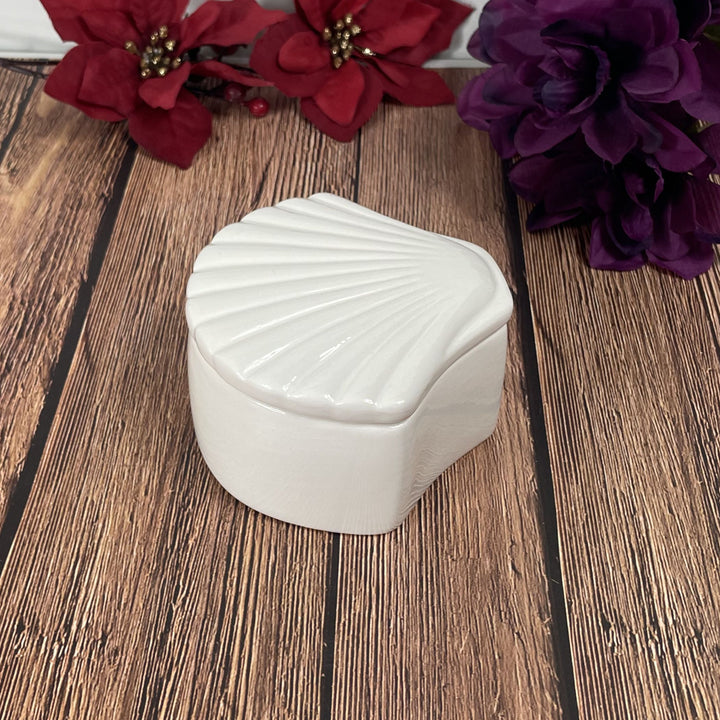 White shell-shaped container on a wooden surface with red and purple flowers in the background