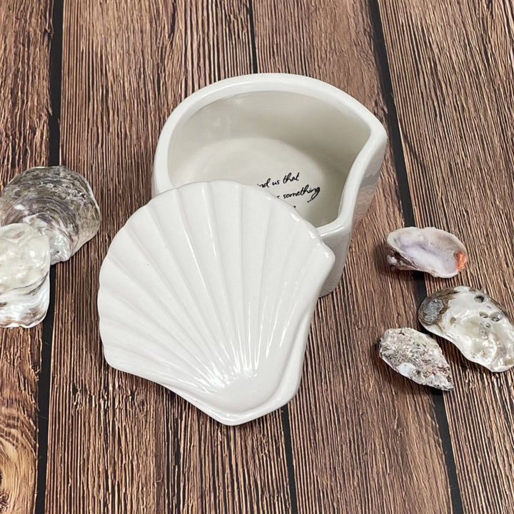 Shell-shaped white ceramic box on a wooden surface with seashells around it.