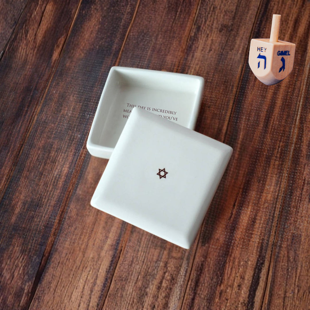 Two white ceramic containers with star designs on a wooden surface, next to a wooden dreidel.