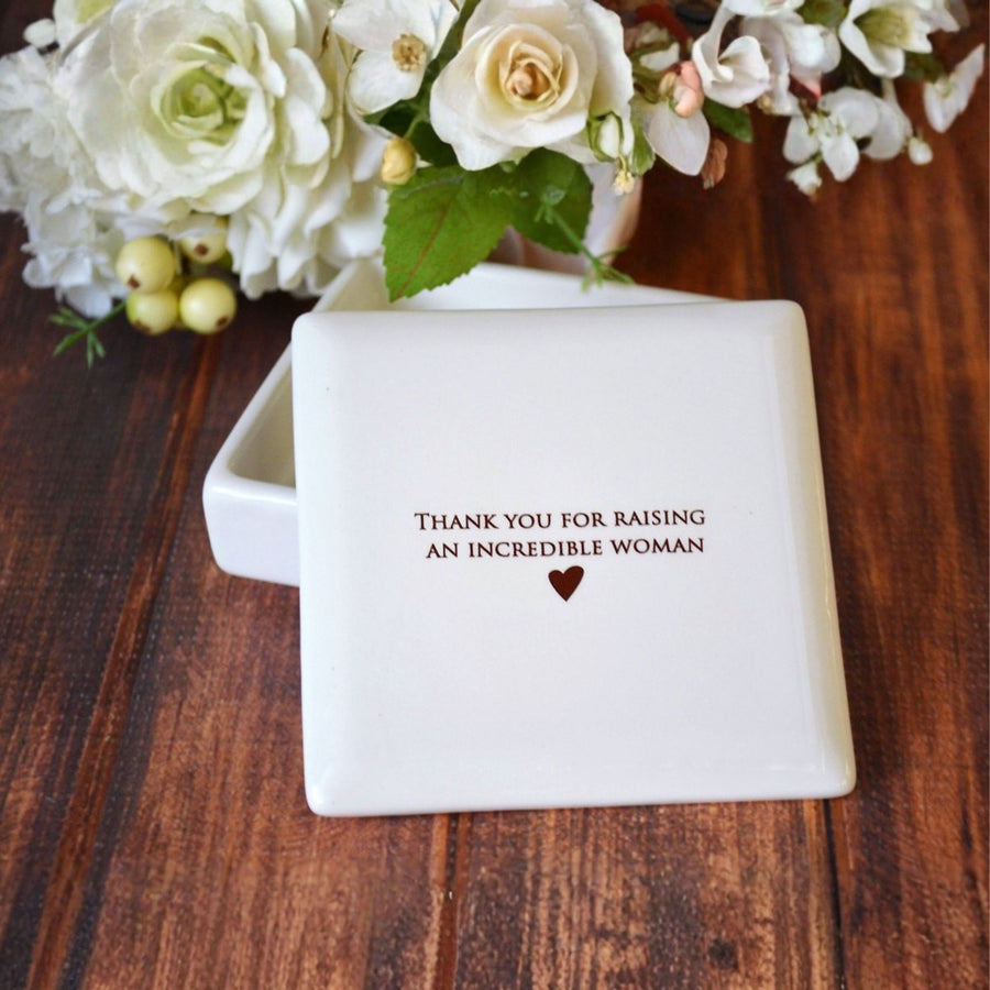 White box with 'Thank you for raising an incredible woman' message on a wooden surface with flowers.