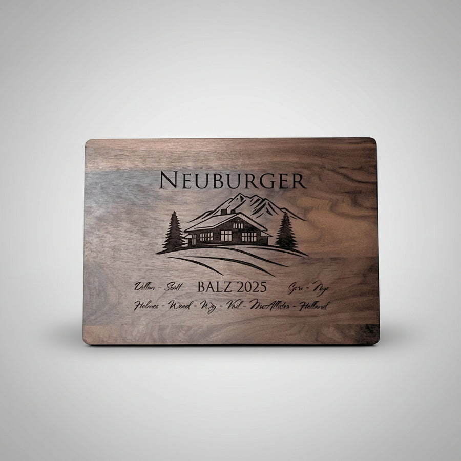 Wooden cutting board with engraved cabin design and text on a white background