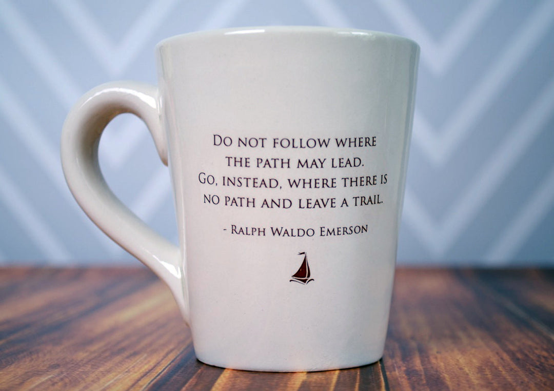 White mug with a quote by Ralph Waldo Emerson on a wooden surface with a blurred background